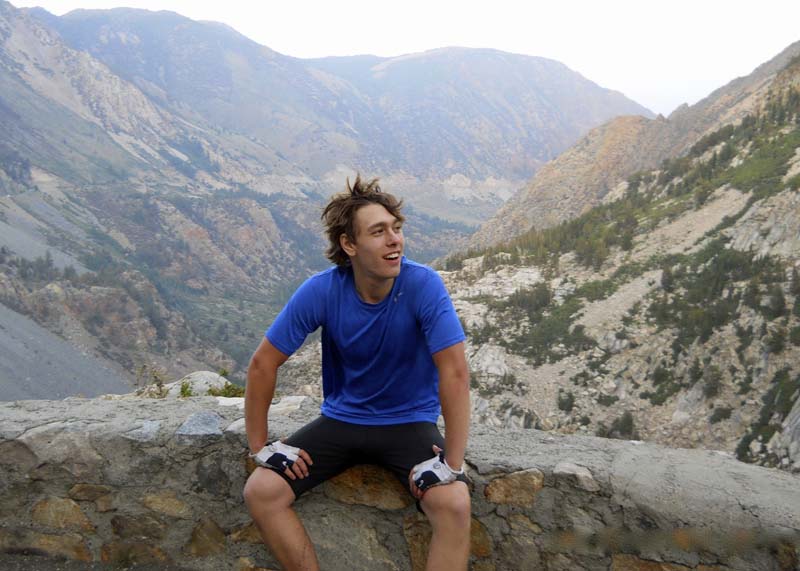 Young man sitting on stone ledge above mountain view