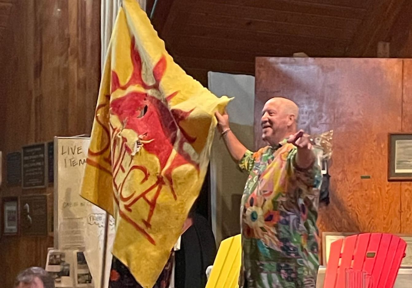 Squeak, a man in a brightly colored shirt, holds up a yellow blanket with Seneca written on it during the live auction
