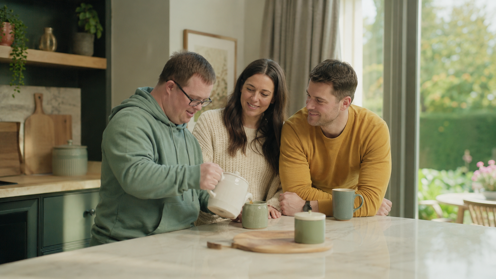 Adult man with Down syndrome preparing tea at home with two supportive adult family members.