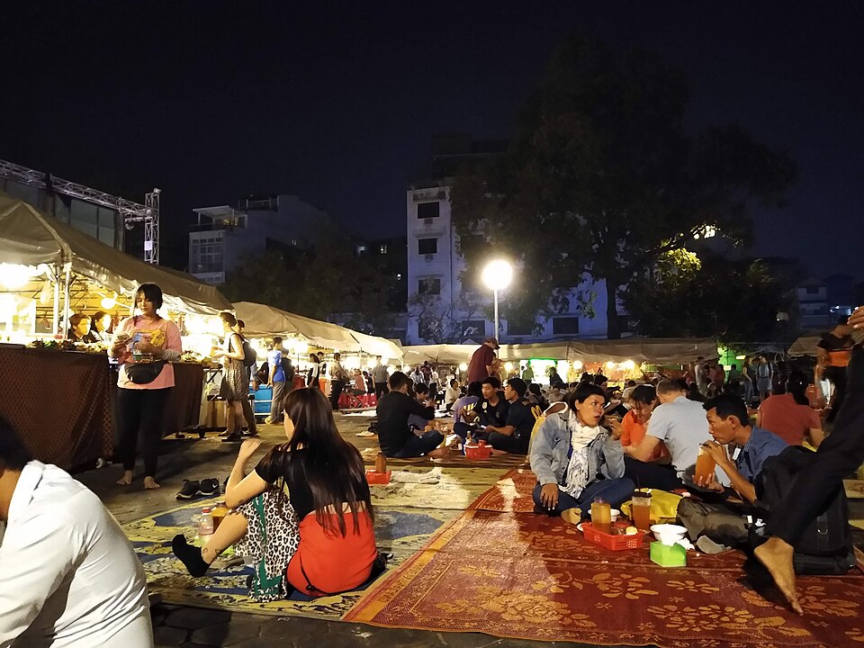 Visiteurs installés sur des nattes devant les stands de nourriture du marché de nuit de Phnom Penh