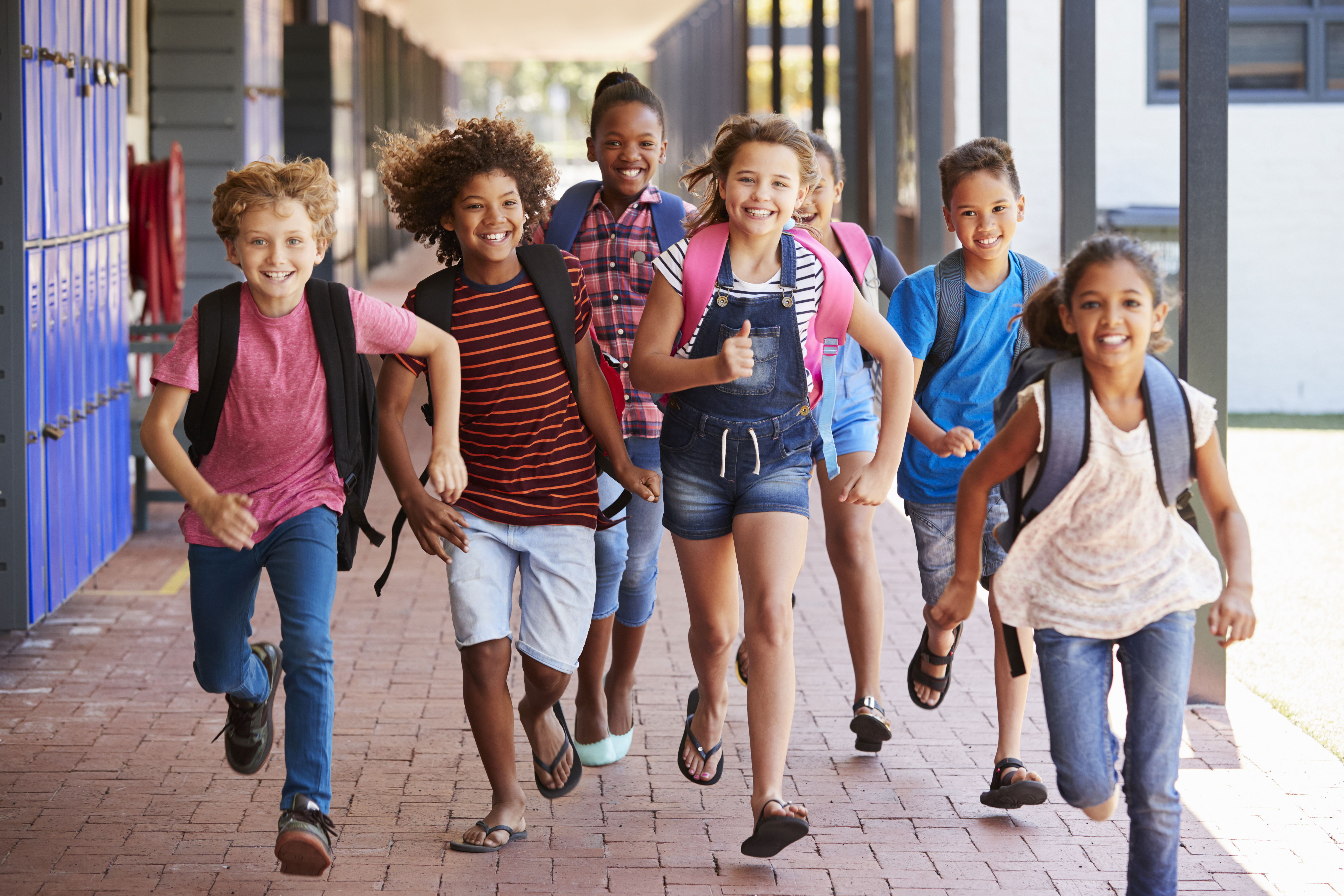 Des enfants en élémentaire souriants, portant leurs cartables et courant, illustrant l’épanouissement et la capacité à surmonter les défis grâce à la sophrologie. 