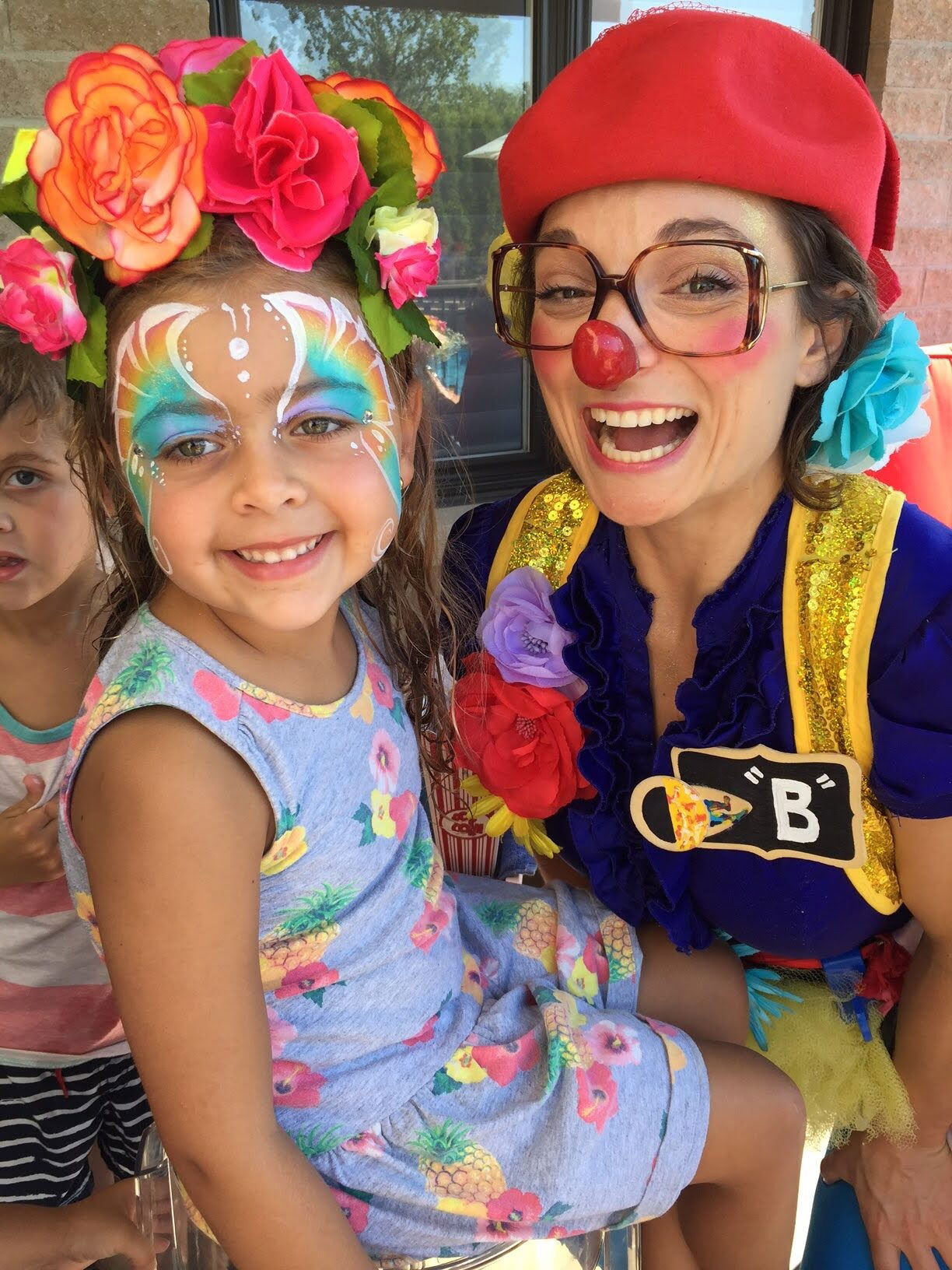 Toddler clown with a smiling child wearing butterfly face paint at a Toronto daycare event
