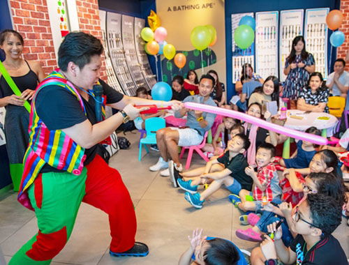 Daycare magician doing a silly balloon trick with a child in front of a group of laughing kids in Toronto