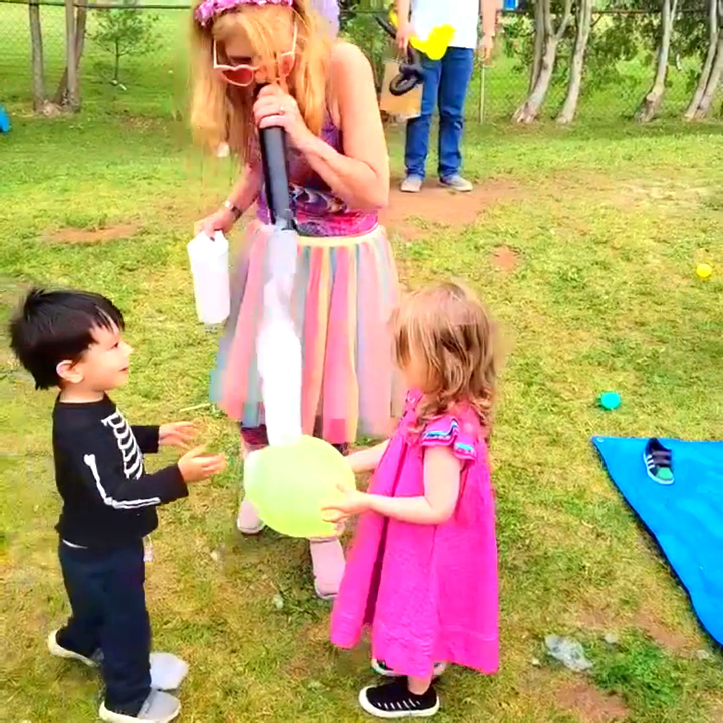 Entertainer making a stream of bubbles for two toddlers holding a balloon during an outdoor daycare bubble show in Toronto