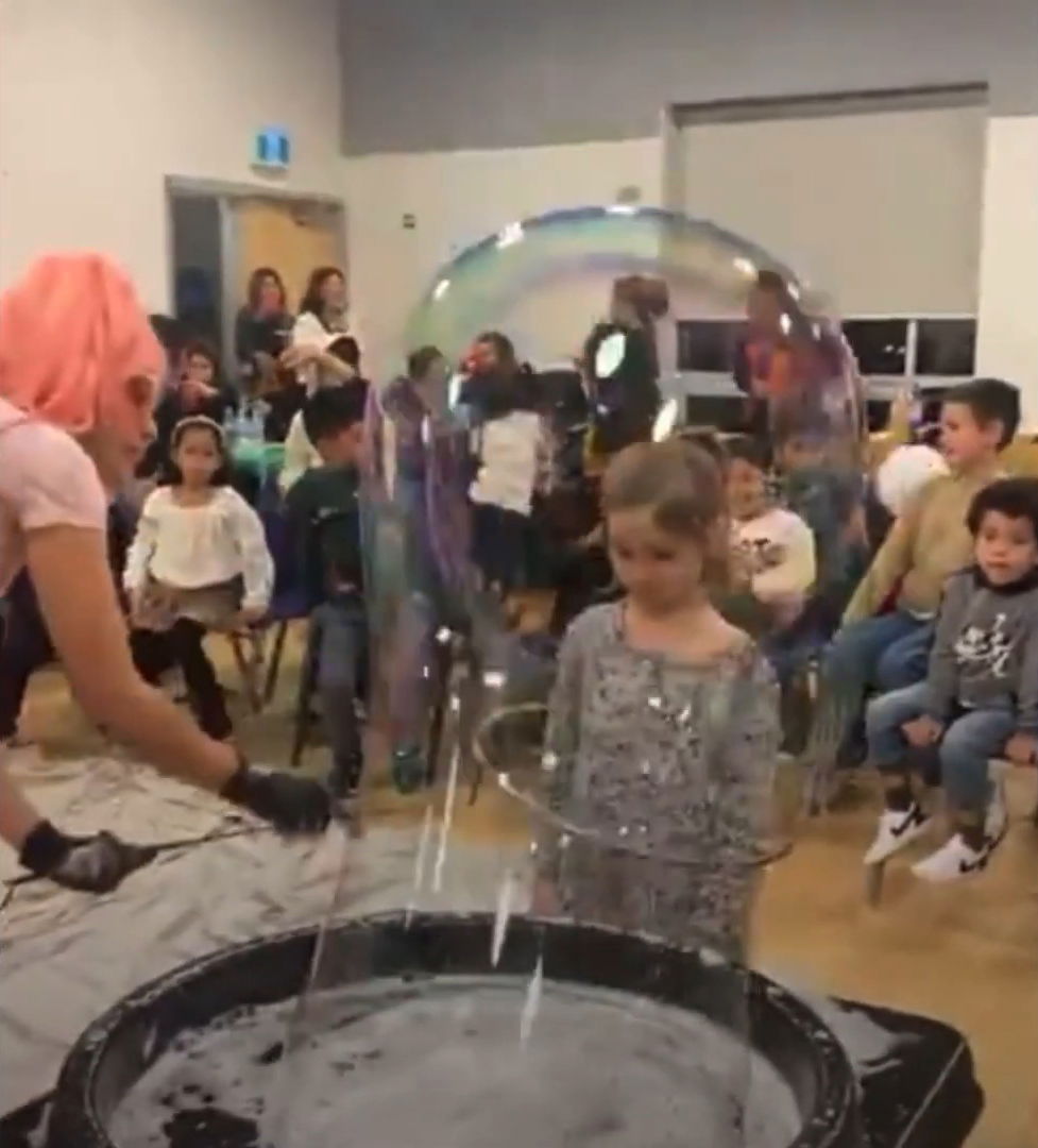 Entertainer creating a giant bubble around a child during an indoor daycare bubble show in Toronto