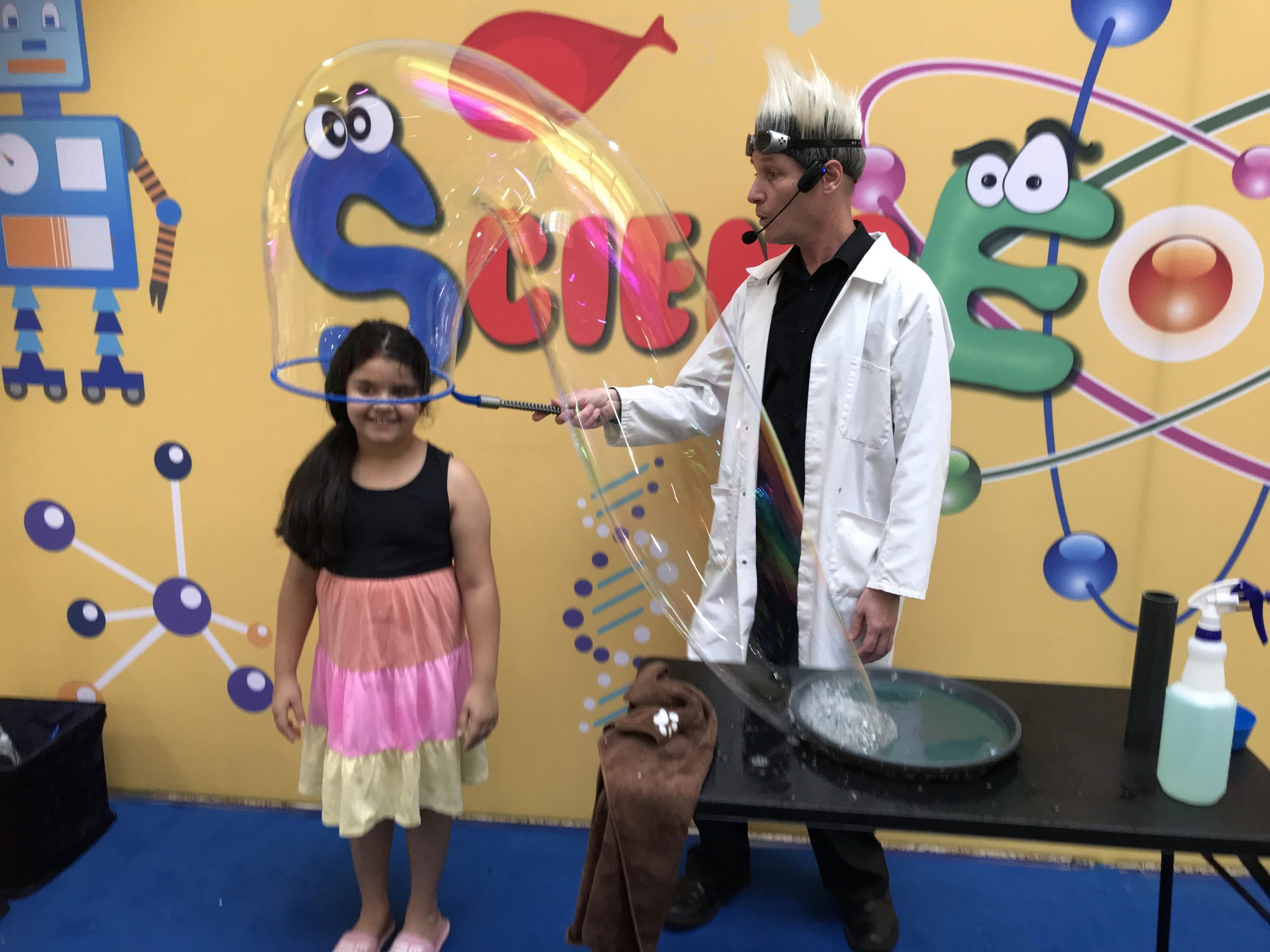 Entertainer in a lab coat putting a giant bubble around a child during a daycare science and bubble show in Toronto