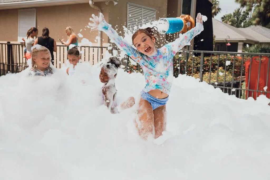 Smiling girl jumping with arms raised in soft foam while other children play during a daycare foam party in Toronto