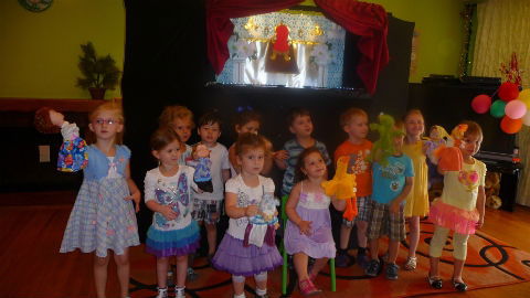 Group of young children holding puppets and posing in front of a puppet stage after a daycare puppet show in Toronto