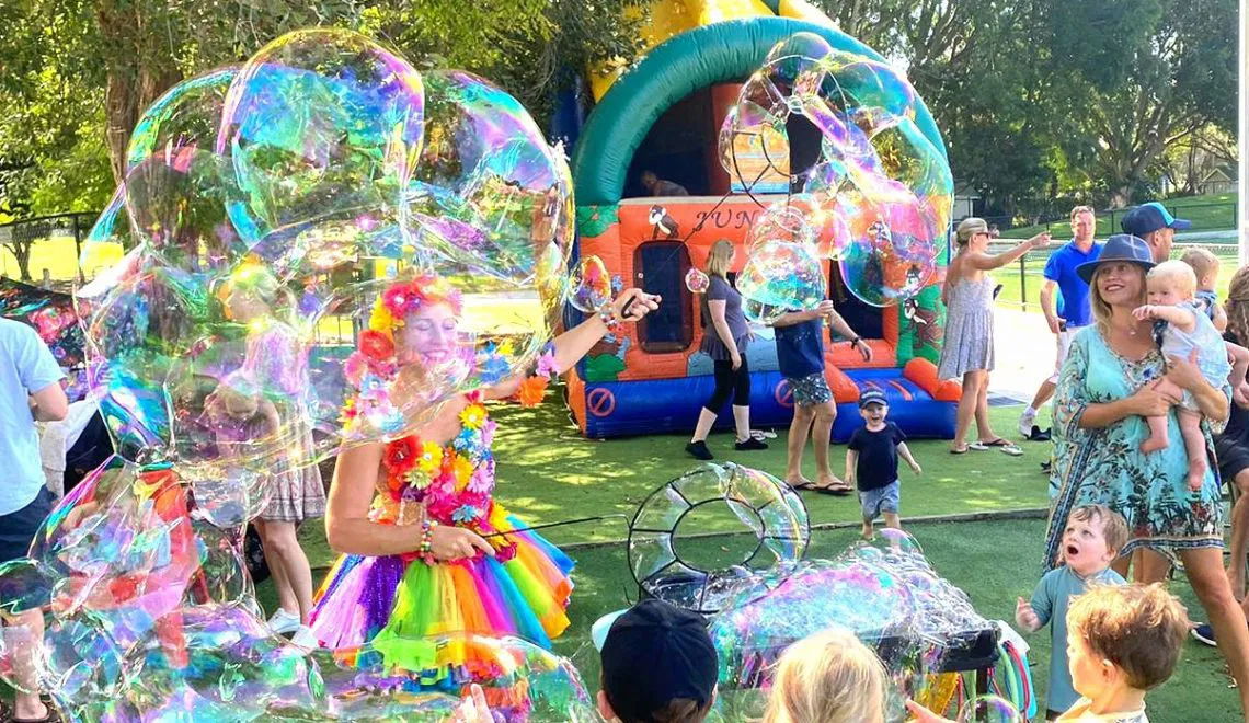 Entertainer in a rainbow costume creating giant bubbles for children at an outdoor kids party in Toronto.
