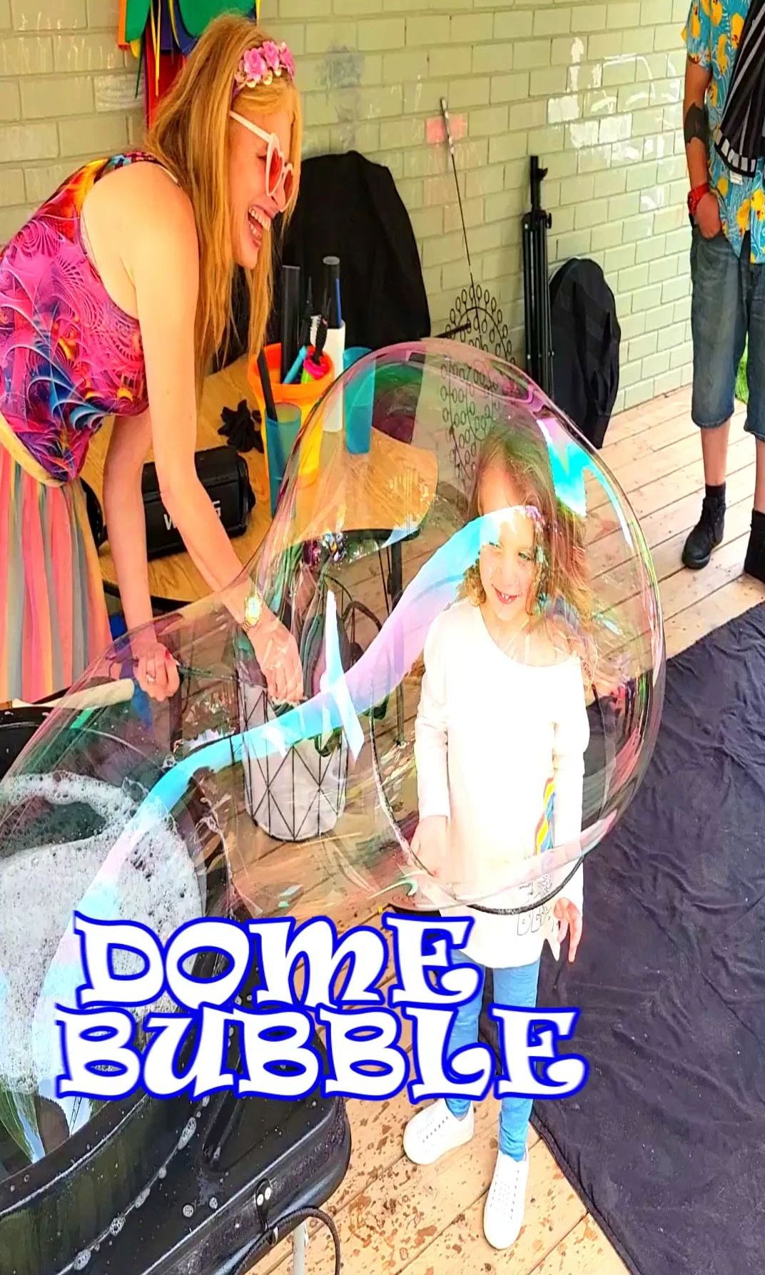 Entertainer placing a giant dome bubble over a smiling child at a kids outdoor bubble party in Toronto.