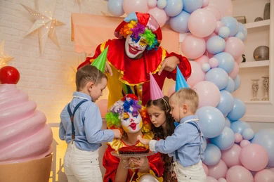 Kids birthday party with a colorful clown entertainer and children gathered around a birthday cake in Toronto.