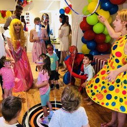 Children enjoying a lively indoor party with a princess entertainer, a clown performer, and a superhero character leading interactive activities.