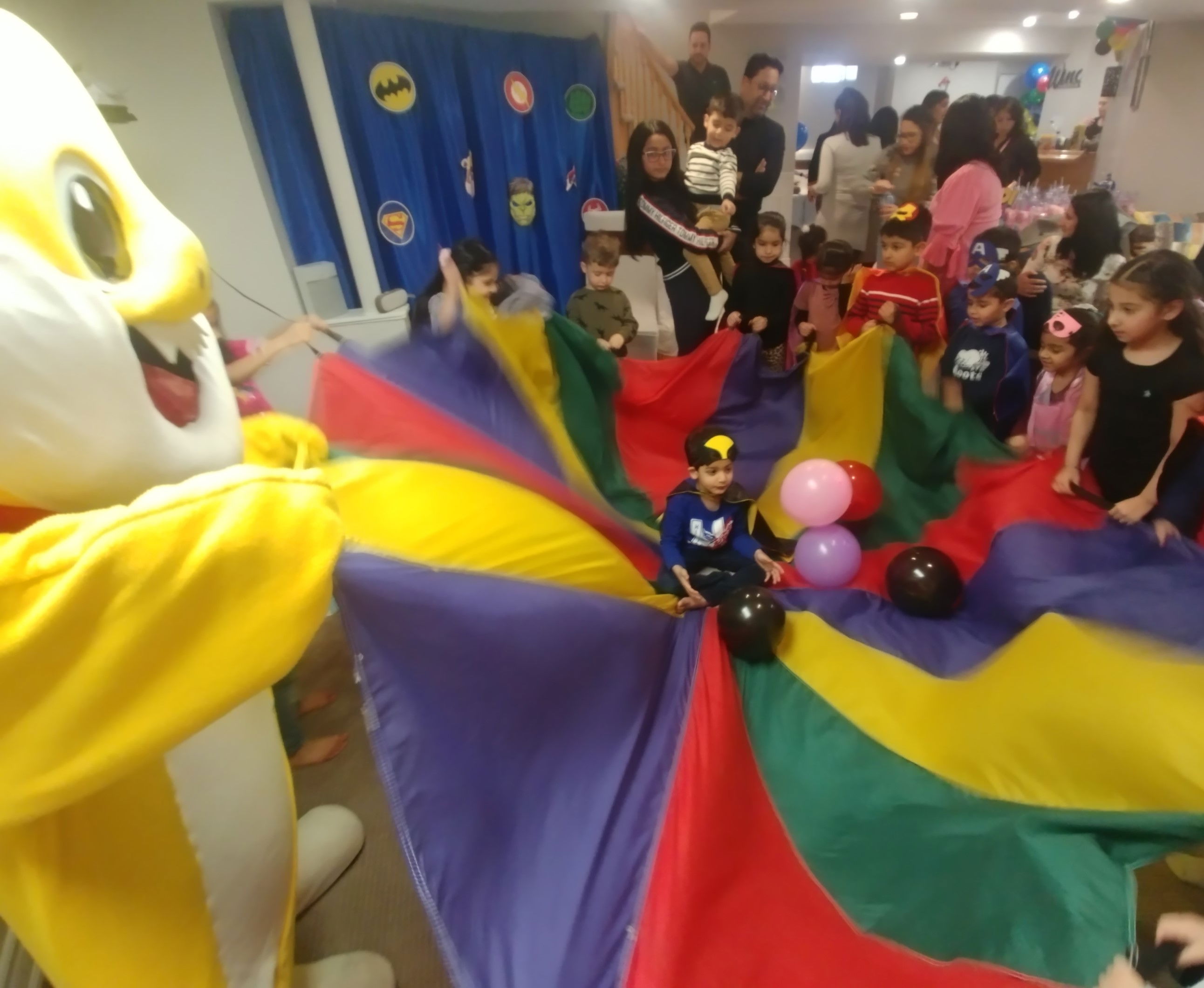 Children playing an interactive parachute game with a mascot entertainer during a lively indoor birthday party.