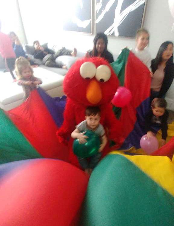 Child hugging a friendly fire dog mascot while sitting on a colorful parachute during a daycare party in Toronto