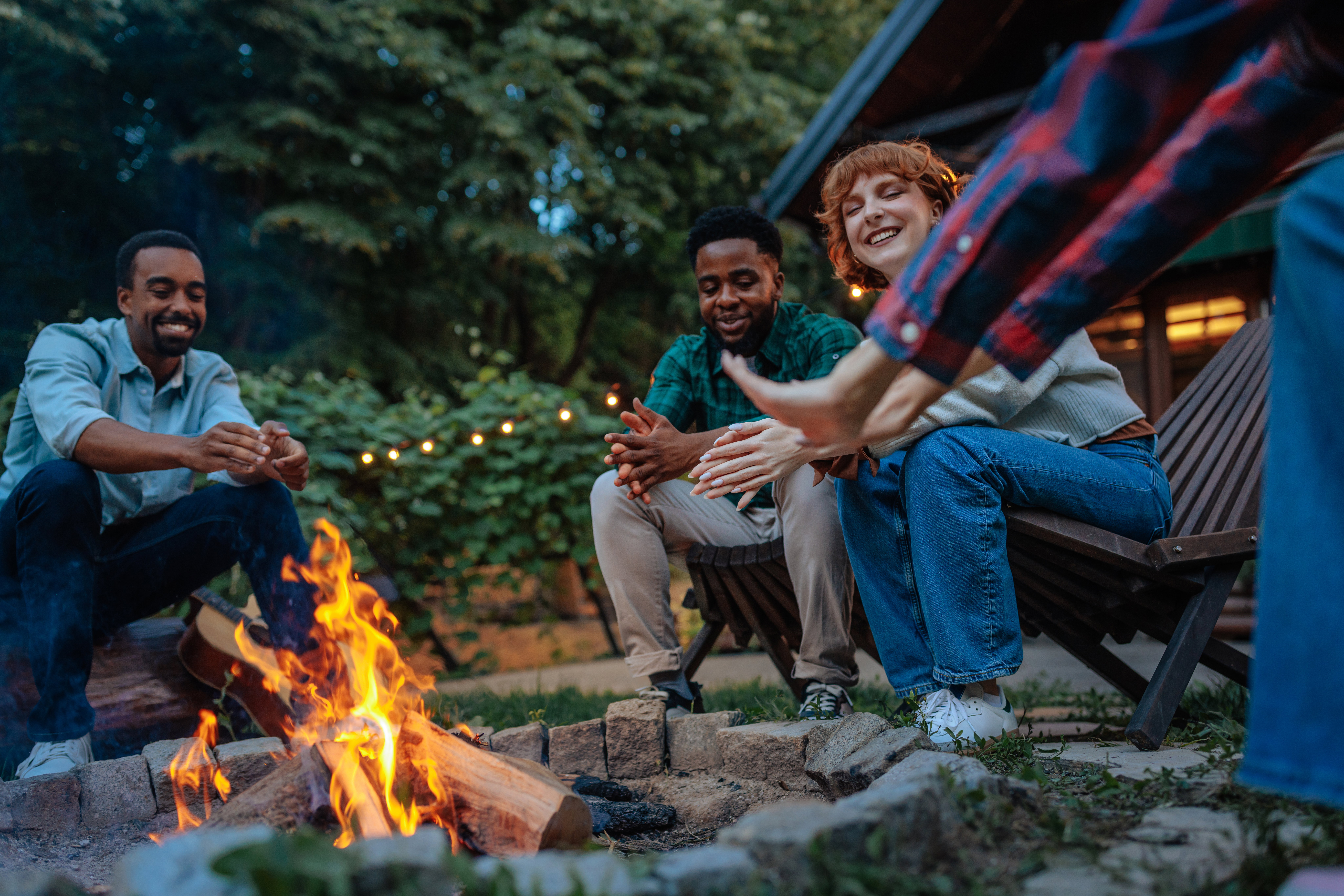 A group of friends in recovery sit sharing stories and laughing around a firepit in backyard of a sober living home.
