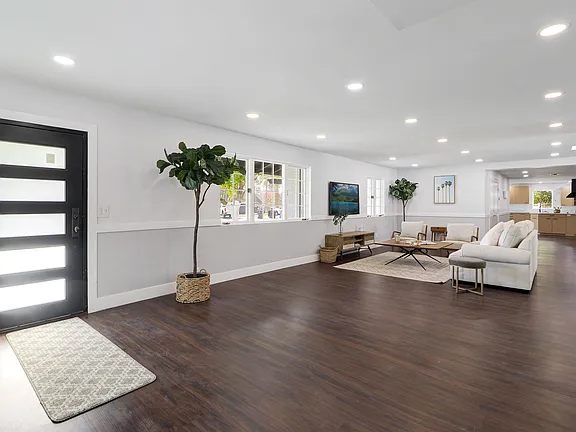 A spacious primary community area just inside the front door showcasing finished wood floors, couch area and open floor space leading to several different corridors of the home. 