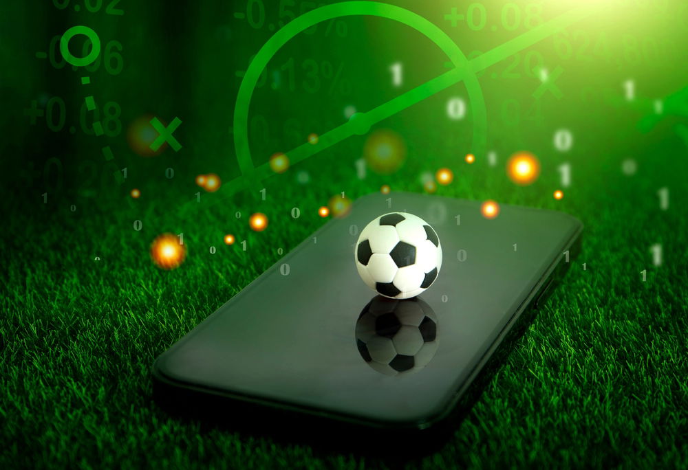 Image of a soccer ball on a mobile device on a green football field turf.