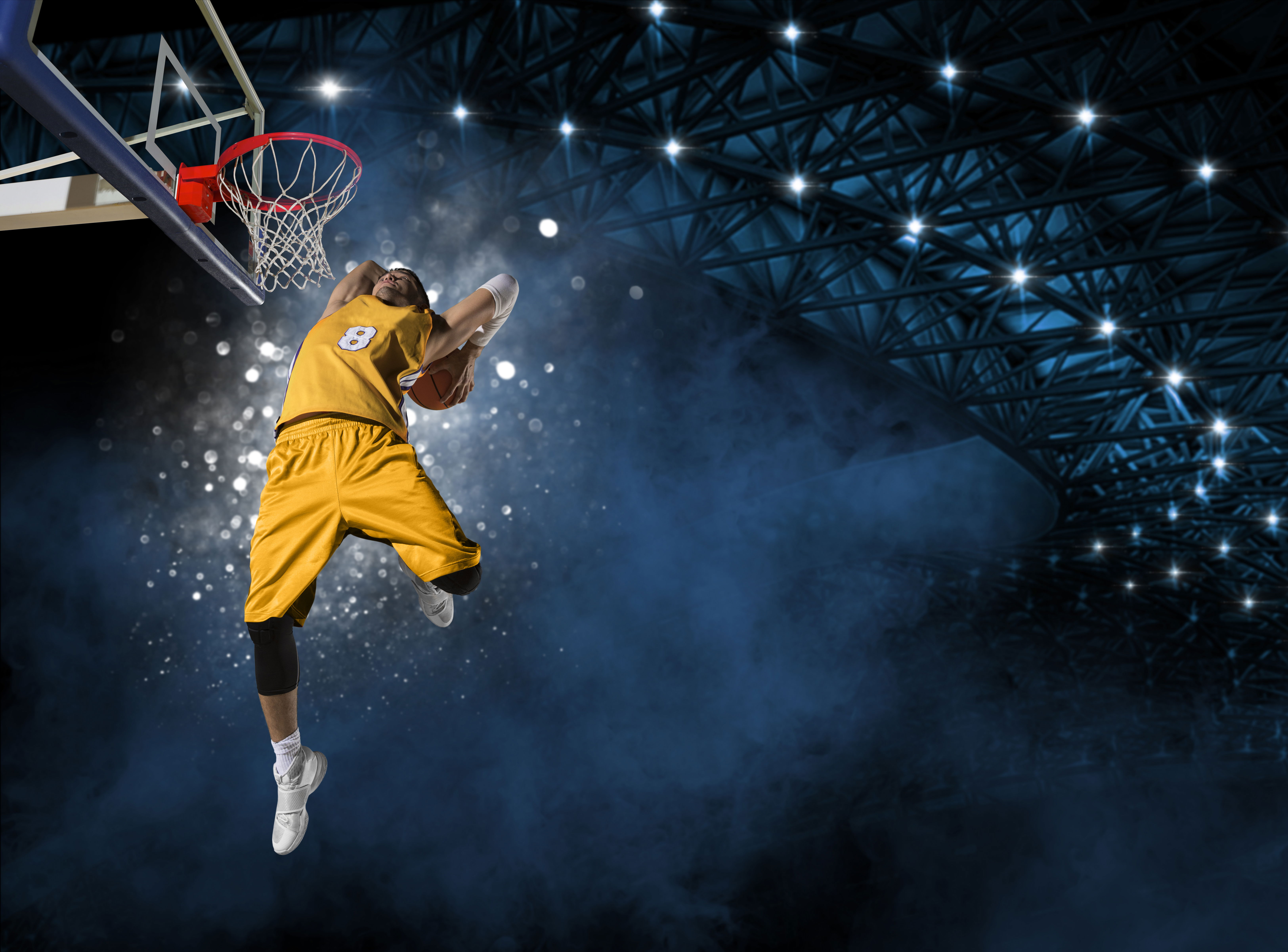 A basketball player dressed in a yellow kit about to dunk a basketball with both hands high above the rim