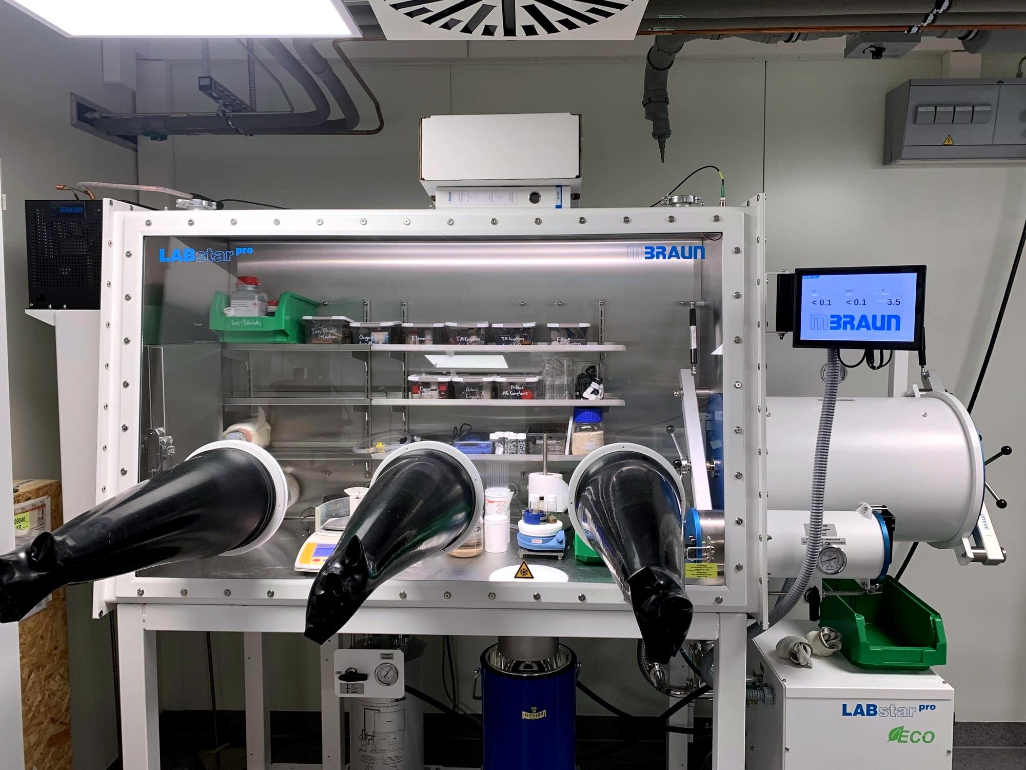 This picture shows a three-glove glovebox with equipment and chemicals inside